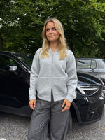 Modelfoto af pige, som bærer EMMA hoodie, lysegrå og MILAN bukser, grå - alt fra BySofieSønderby. Baggrund er p-plads og træer