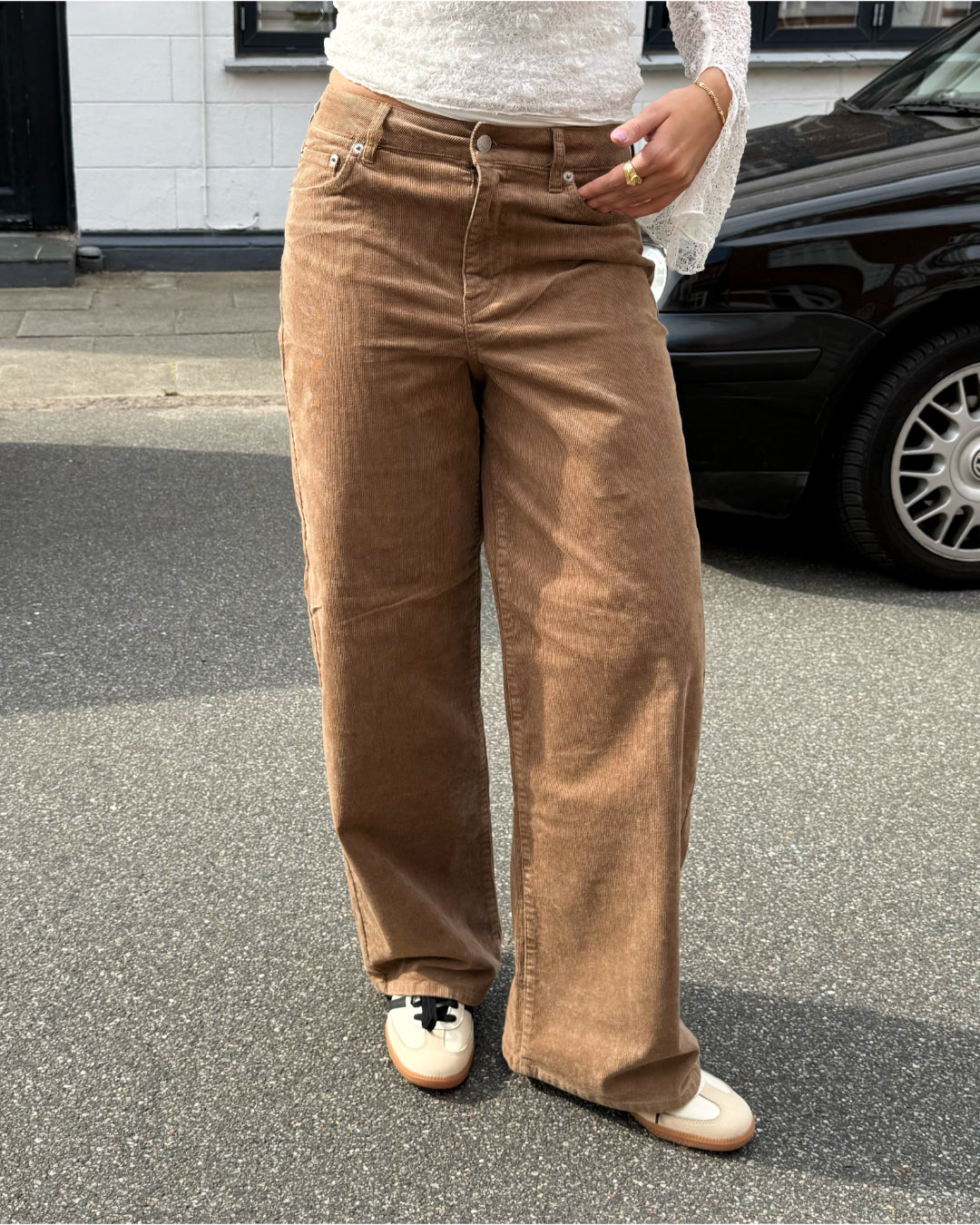 Modelfoto af pige i brune Gelly bukser og en hvid blonde top. Alt er fra BySofieSønderby
