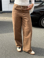 Modelfoto af pige i brune Gelly bukser og en hvid blonde top. Alt er fra BySofieSønderby