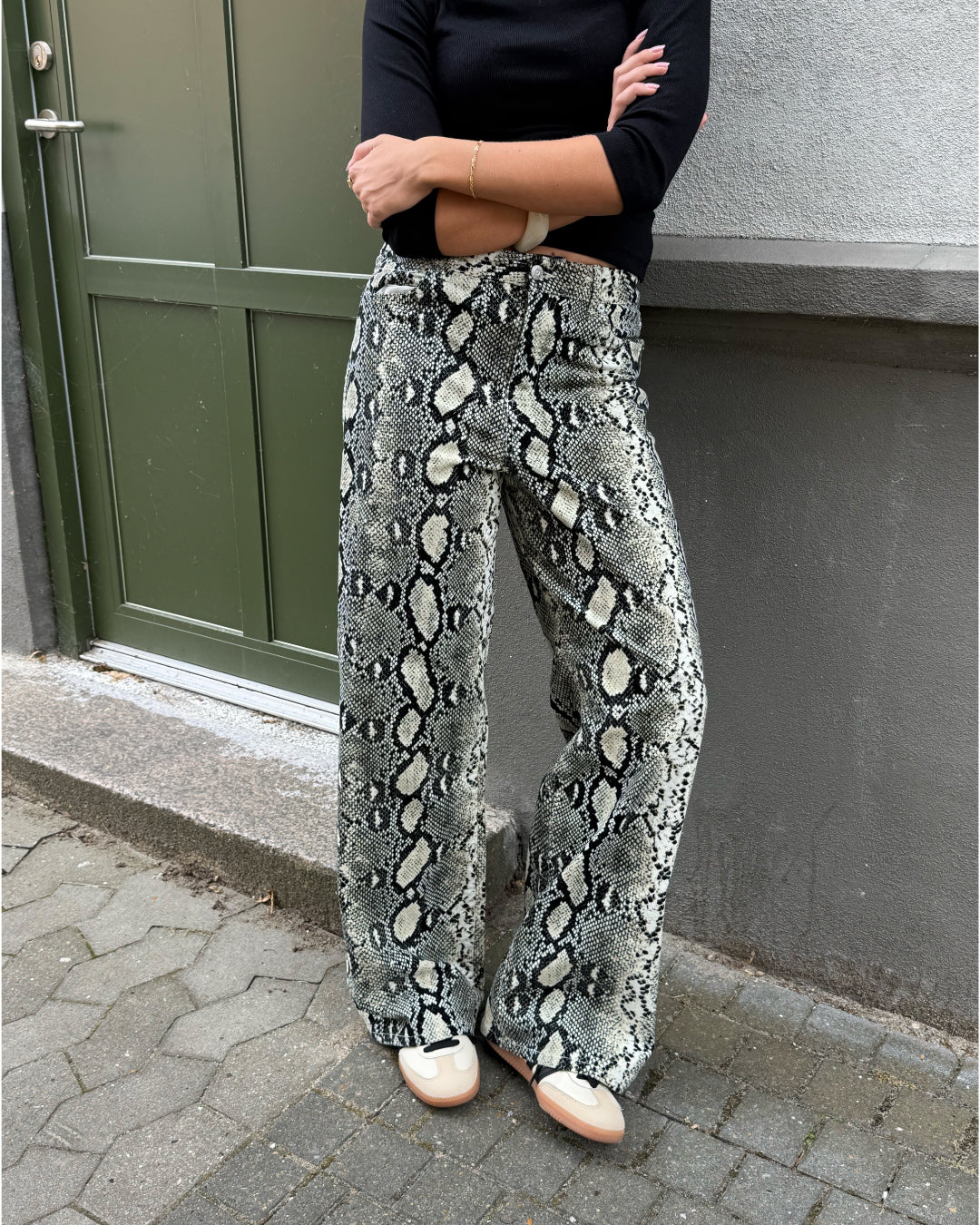 Modelfoto af pige i Gelly bukser med slangeprint, og en sort bluse. Alt er fra BySofieSønderby