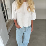 Modelfoto af pige som bærer hvid KAMMA bluse med blomstret sy-mønster, samt lyseblå jeans. Alt er fra BySofieSønderby