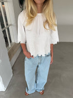 Modelfoto af pige som bærer hvid KAMMA bluse med blomstret sy-mønster, samt lyseblå jeans. Alt er fra BySofieSønderby