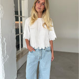 Modelfoto af pige som bærer hvid KAMMA bluse med blomstret sy-mønster, samt lyseblå jeans. Alt er fra BySofieSønderby