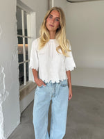 Modelfoto af pige som bærer hvid KAMMA bluse med blomstret sy-mønster, samt lyseblå jeans. Alt er fra BySofieSønderby