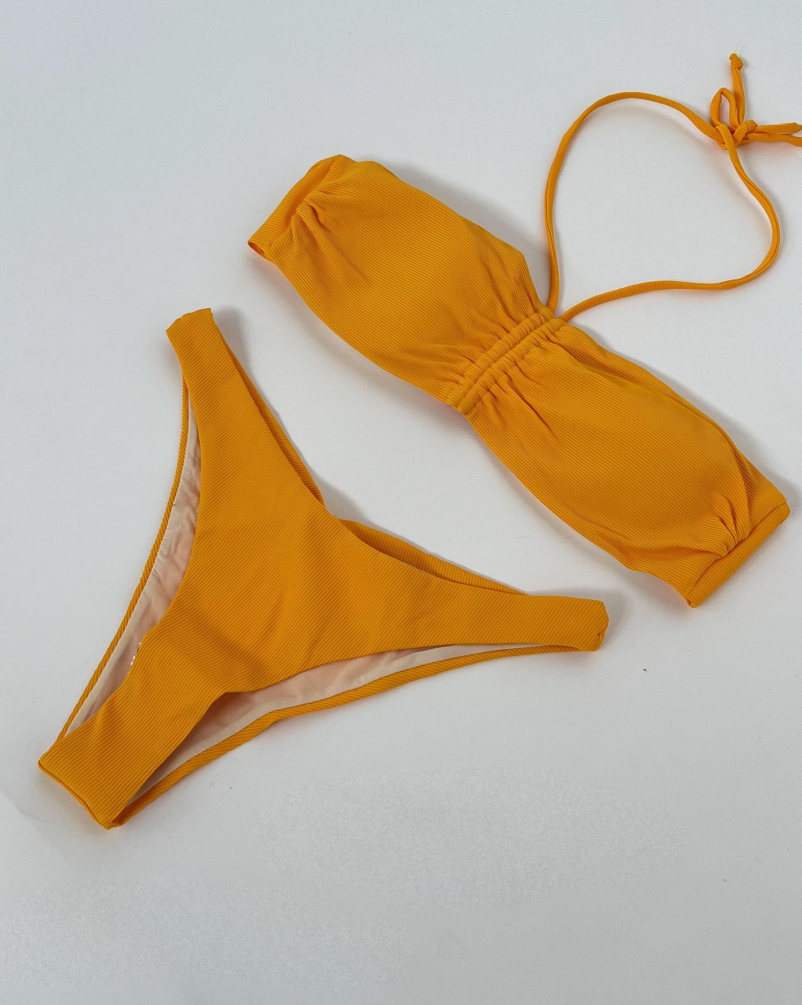 Orange bikini med stropløs top og bindebånd, og matchende bund. Bikinien ligger fladt på en hvid overflade, klar til brug eller fremvisning. Ingen tekst til stede.