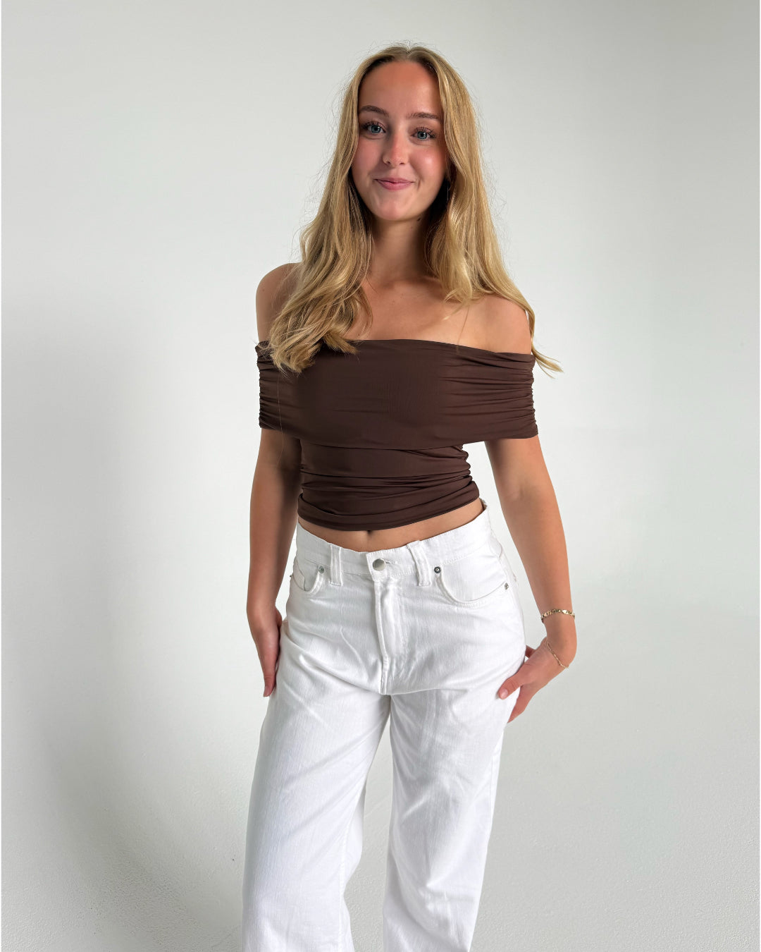Modelfoto af pige som bærer en Leia top i brun, samt et par hvide Nanna jeans. Alt fra By Sofie Sønderby