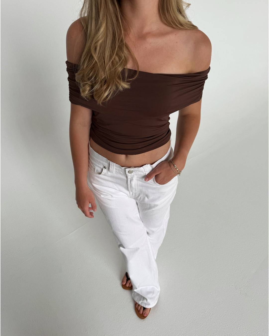 Modelfoto af pige som bærer en Leia top i brun, samt et par hvide Nanna jeans. Alt fra By Sofie Sønderby