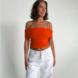 Modelfoto af pige som bærer en Leia top i orange, samt et par hvide Nanna jeans. Alt fra By Sofie Sønderby