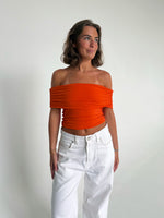Modelfoto af pige som bærer en Leia top i orange, samt et par hvide Nanna jeans. Alt fra By Sofie Sønderby