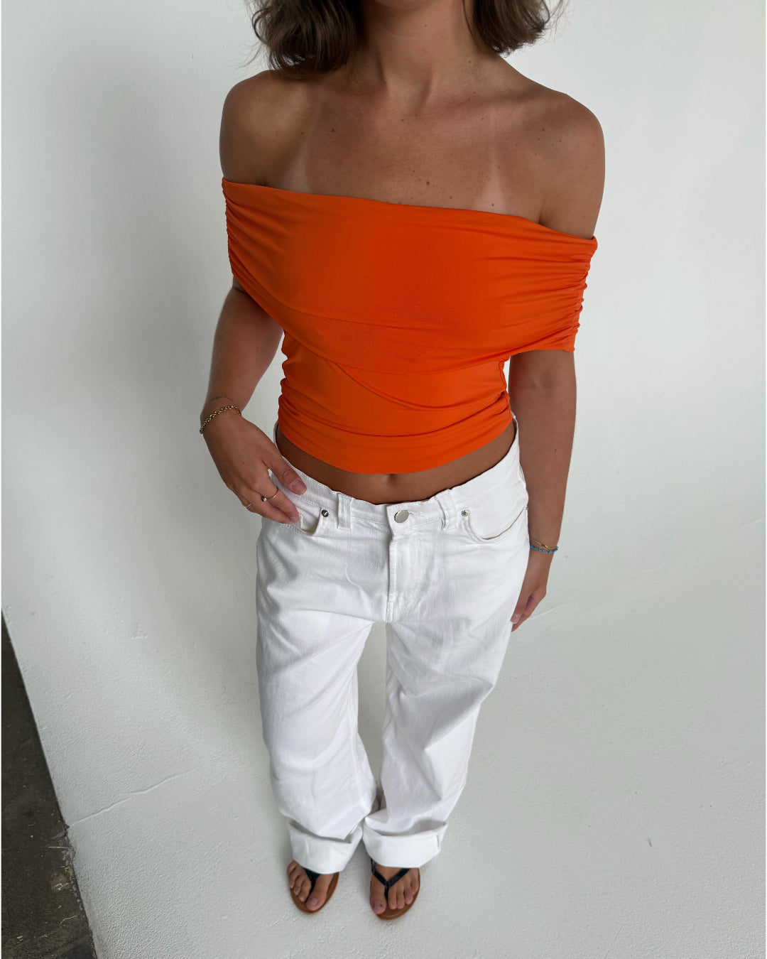 Modelfoto af pige som bærer en Leia top i orange, samt et par hvide Nanna jeans. Alt fra By Sofie Sønderby