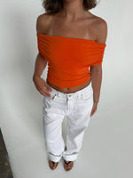 Modelfoto af pige som bærer en Leia top i orange, samt et par hvide Nanna jeans. Alt fra By Sofie Sønderby