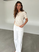 Modelfoto af pige som bærer en LILLIANA beigestribet polo t-shirt og hvide jeans. Alt er fra BySofieSønderby