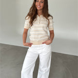 Modelfoto af pige som bærer en LILLIANA beigestribet polo t-shirt og hvide jeans. Alt er fra BySofieSønderby