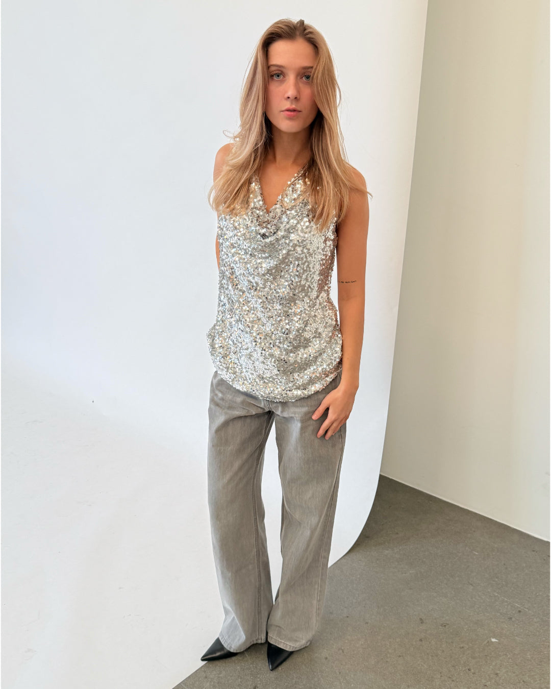 Modelfoto af pige i sølvfarvet LINA top med pailetter, samt grå NANNA jeans. Alt er fra BySofieSønderby.