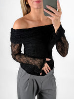 Modelfoto af pige i sort MAISY off-shoulder blondebluse og grå LISA bukser. Alt er fra BySofieSønderby.