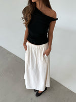 Modelfoto af pige som bærer en sort oneshoulder MILENA top, samt en hvid nederdel og sorte ballerinasko. Alt er fra BySofieSønderby