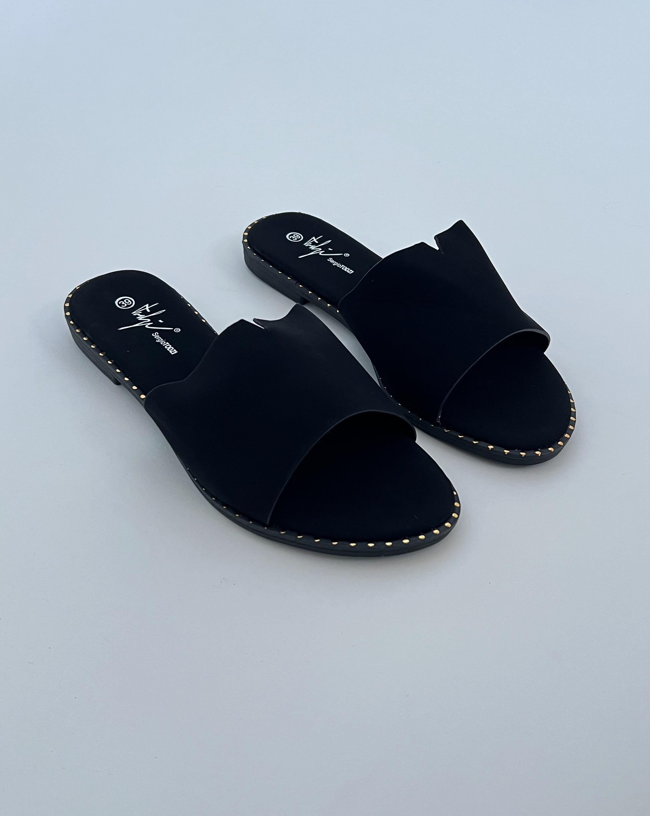 Sorte sandaler ligger på en flad overflade. De har brede stropper og små guldnitter langs sålen. Tekst på indersål: "39," "Hyji," "supermodo."