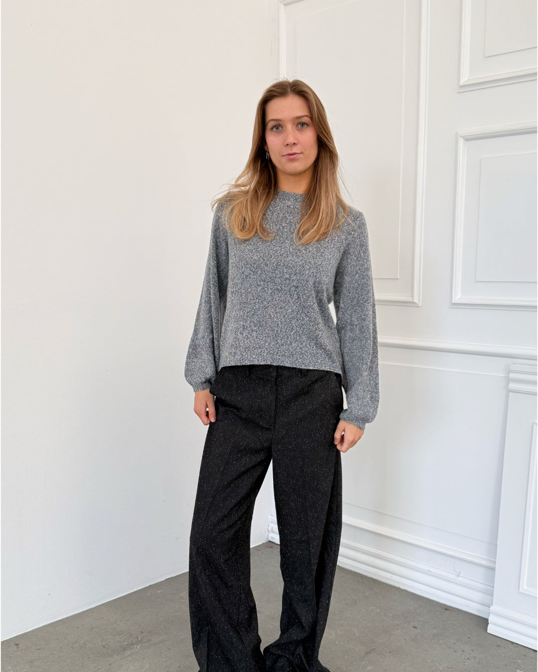 Modelfoto af pige i grå PATRICE strik, samt sortmelerede ELLIS bukser. Alt er fra BySofieSønderby.