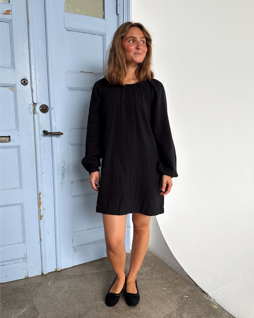 Modelfoto af pige som bærer en Pia kjole i sort, samt et par sorte Regina ballerinaer. Alt fra By Sofie Sønderby