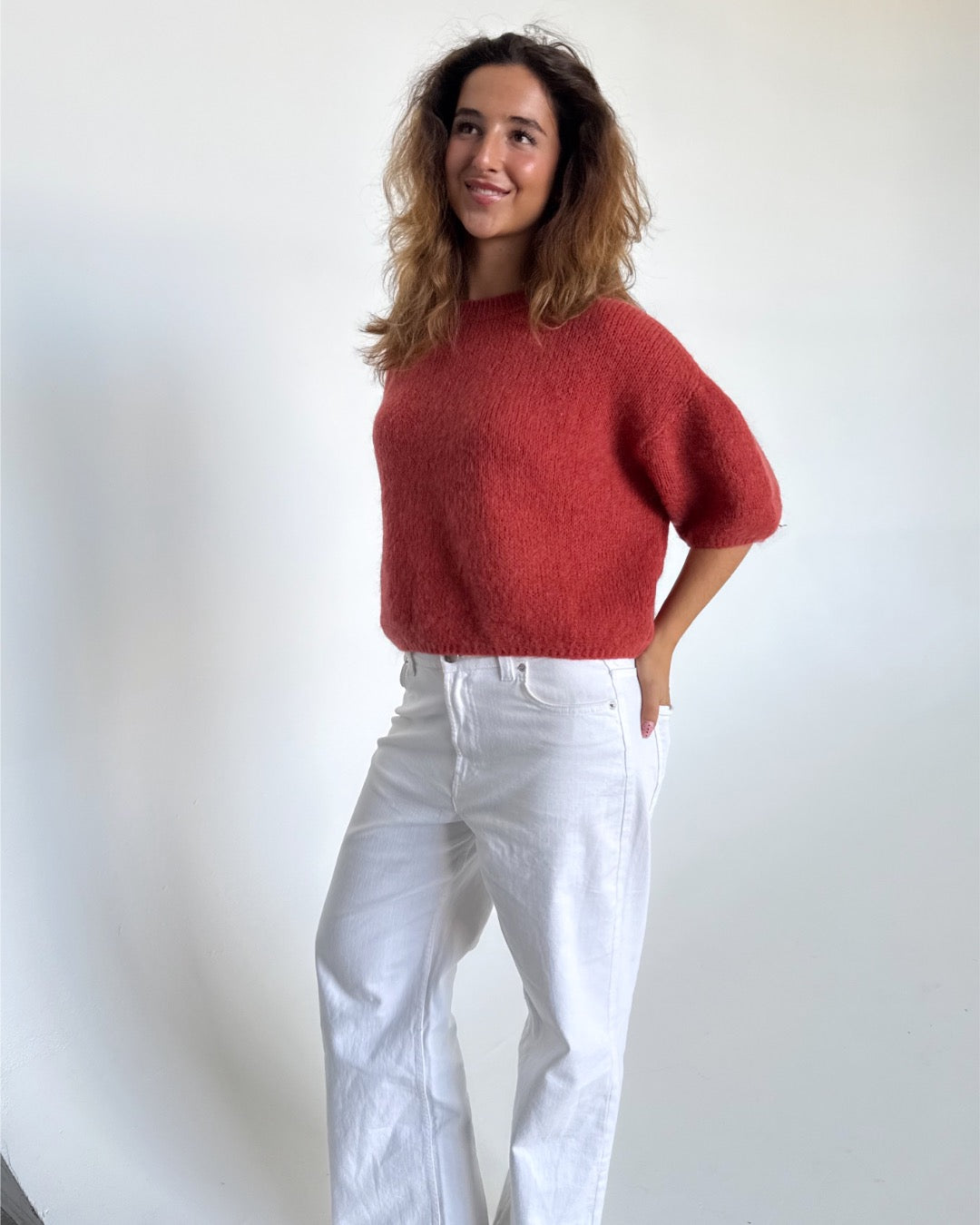 Modelfoto af pige i terracottafarvet Poppy strik t-shirt og hvide Nanna jeans. Alt er fra BySofieSønderby