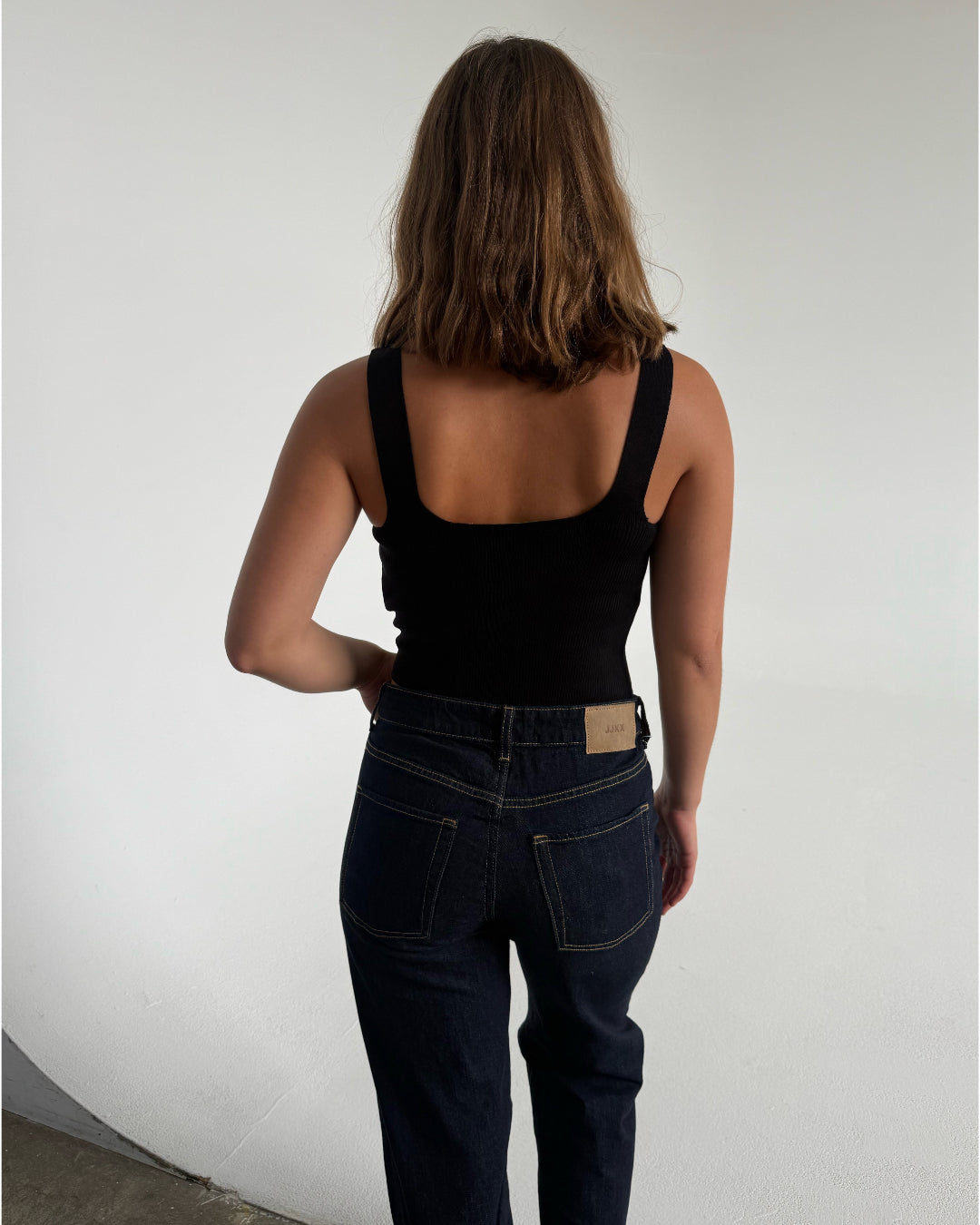 Modelfoto af pige som bærer en Posie top i sort, samt et par mørkeblå jeans. Alt fra By Sofie Sønderby