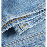 Blå denimstof ligger foldet med synlige gulbrune syninger. Stoffet er ru med let slidte kanter, hvilket er typisk for jeansmateriale.