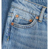 Et par blå jeans ligger fladt, med fokus på lommen dekoreret med kobbernitter. Synlige sømme og detaljer viser stoffets struktur i et enkel og tidløst design.