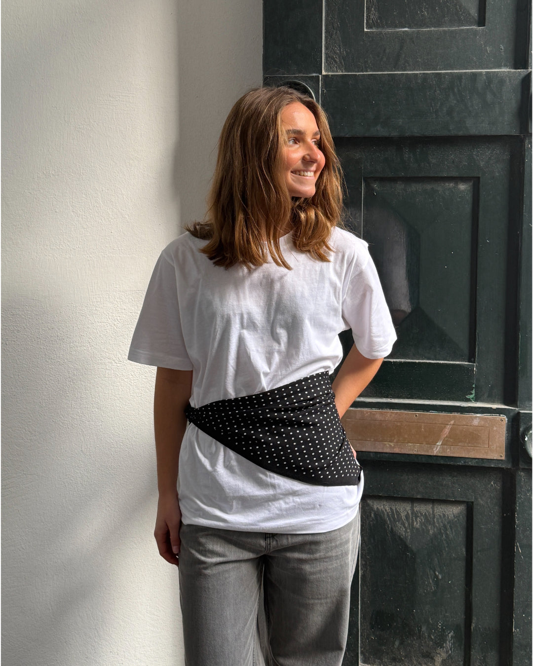 Modelfoto af pige i sort ROSALINA tørklæde bundet uden på hvid basic t-shirt. Bukserne er grå NANNA jeans. Alt er fra BySofieSønderby.