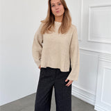 Modelfoto af pige i creme SIGGA strik, samt sortmelerede ELLIS bukser. Alt er fra BySofieSønderby.