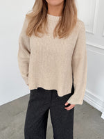 Modelfoto af pige i creme SIGGA strik, samt sortmelerede ELLIS bukser. Alt er fra BySofieSønderby.