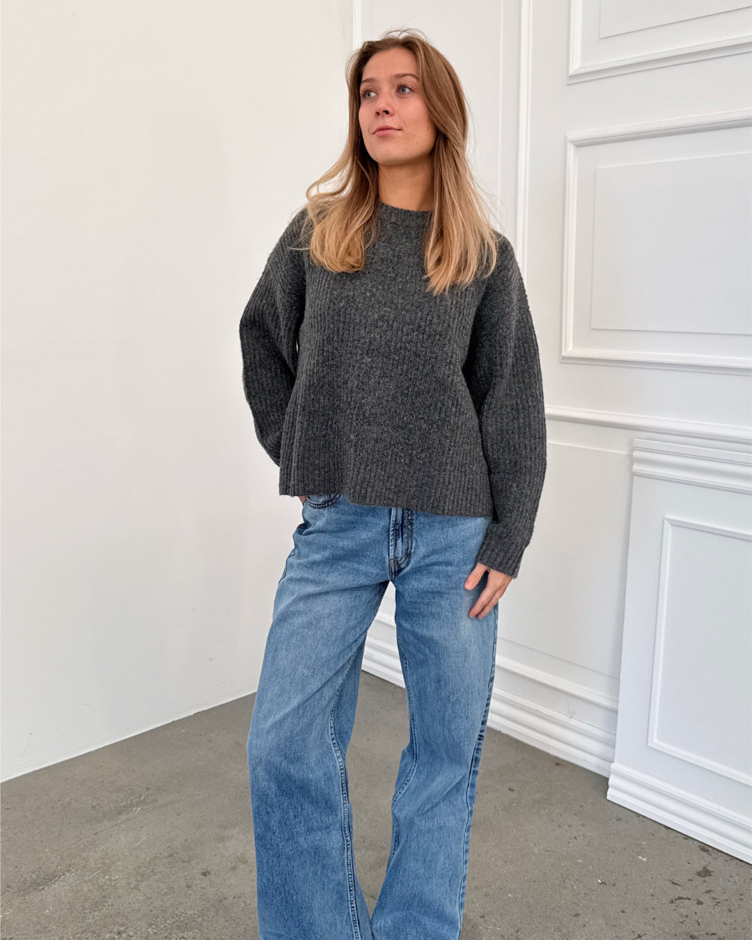 Modelfoto af pige i grå SIGGA strik, samt blå NANNA jeans. Alt er fra BySofieSønderby.