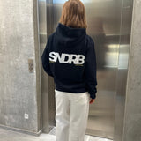 Stemningsbillede af pige der bærer en navy hoodie med hvidt SNDRB tryk og hvide NANNA jeans.  Fra BySofieSønderby