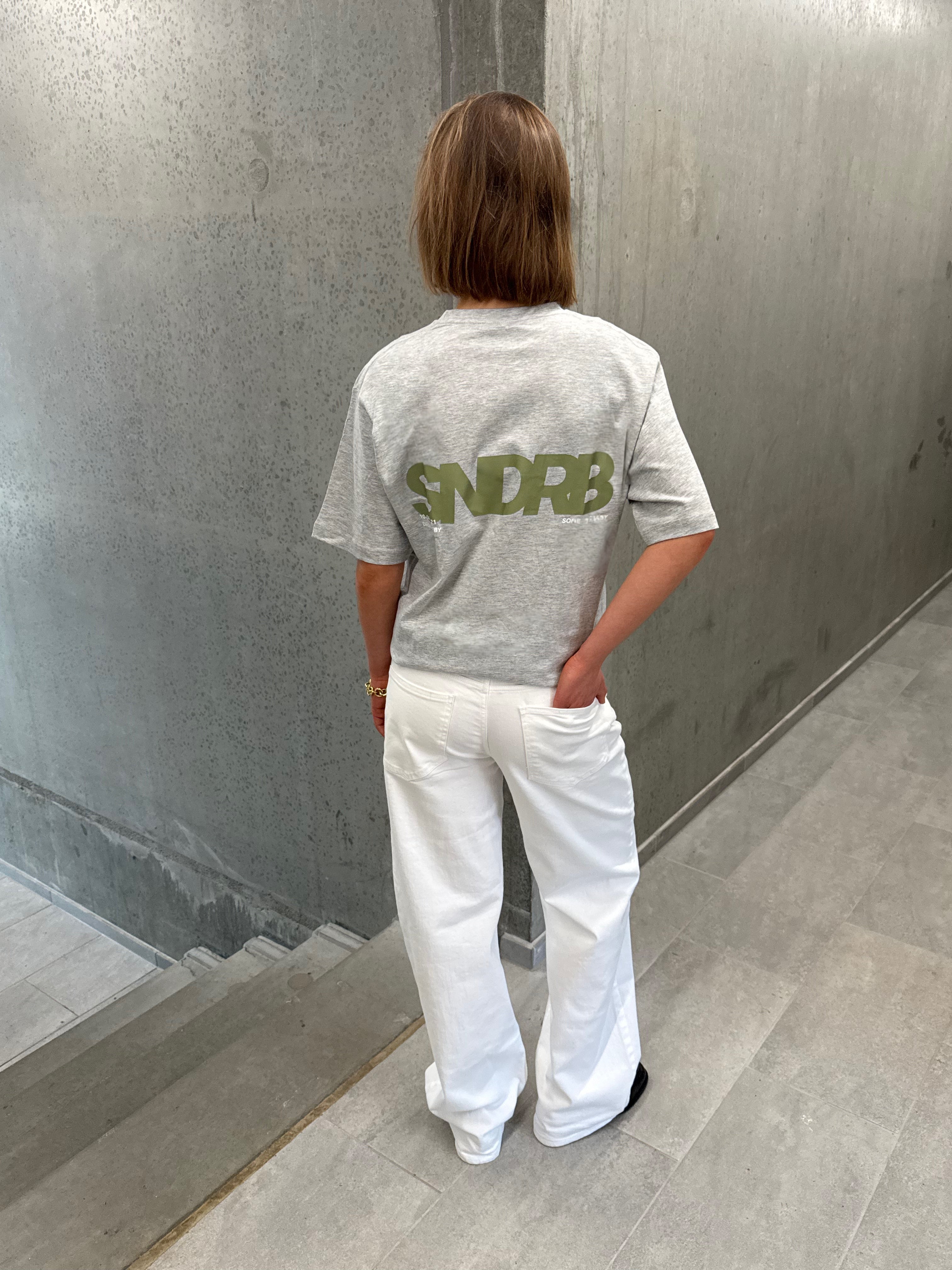 Stemningsbillede af pige der bærer en grå t-shirt med army SNDRB tryk og hvide NANNA jeans.  Fra BySofieSønderby