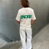 Stemningsbillede af pige der bærer en hvid t-shirt med grønt SNDRB tryk og blå NANNA jeans.  Fra BySofieSønderby