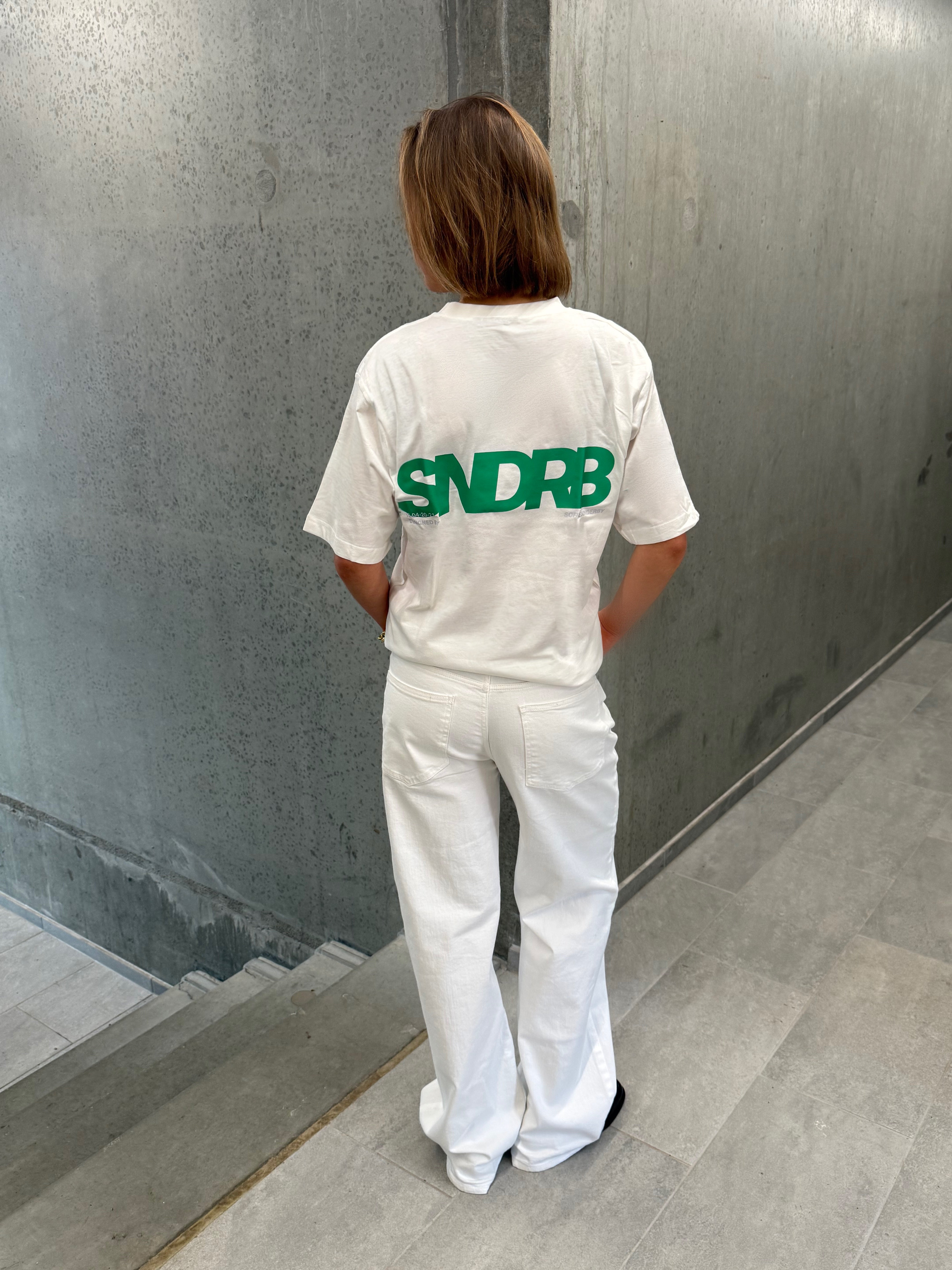 Stemningsbillede af pige der bærer en hvid t-shirt med grønt SNDRB tryk og blå NANNA jeans.  Fra BySofieSønderby