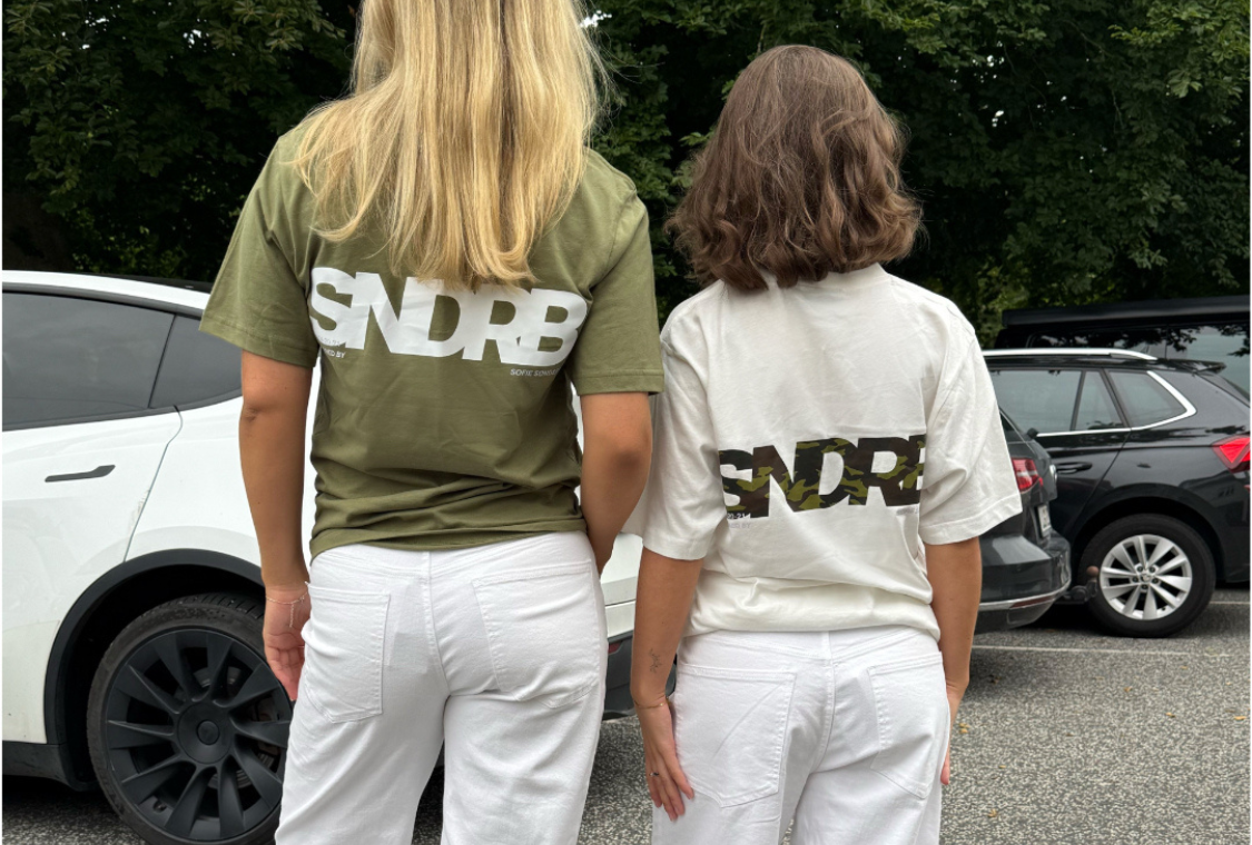 Modelbillede af piger i SNDRB t-shirts, den ene i army med hvid tryk, den anden i hvid t-shirt med camouflagetryk. Begge i hvide jeans. Alt er fra BySofieSønderby