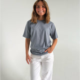 Modelfoto af pige som bærer en SNDRB tee i farven stone, samt et par hvide jeans. Alt fra By Sofie Sønderby