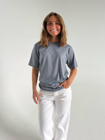 Modelfoto af pige som bærer en SNDRB tee i farven stone, samt et par hvide jeans. Alt fra By Sofie Sønderby