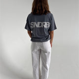 Modelfoto af pige som bærer en SNDRB tee i farven stone, samt et par hvide jeans. Alt fra By Sofie Sønderby
