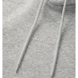 Detaljefoto af fronten på en Studio Vesterbro hoddie i lysgrå, hvor man ser skriften JJXX STUDIO. Fra BySofieSønderby