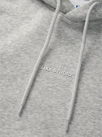 Detaljefoto af fronten på en Studio Vesterbro hoddie i lysgrå, hvor man ser skriften JJXX STUDIO. Fra BySofieSønderby
