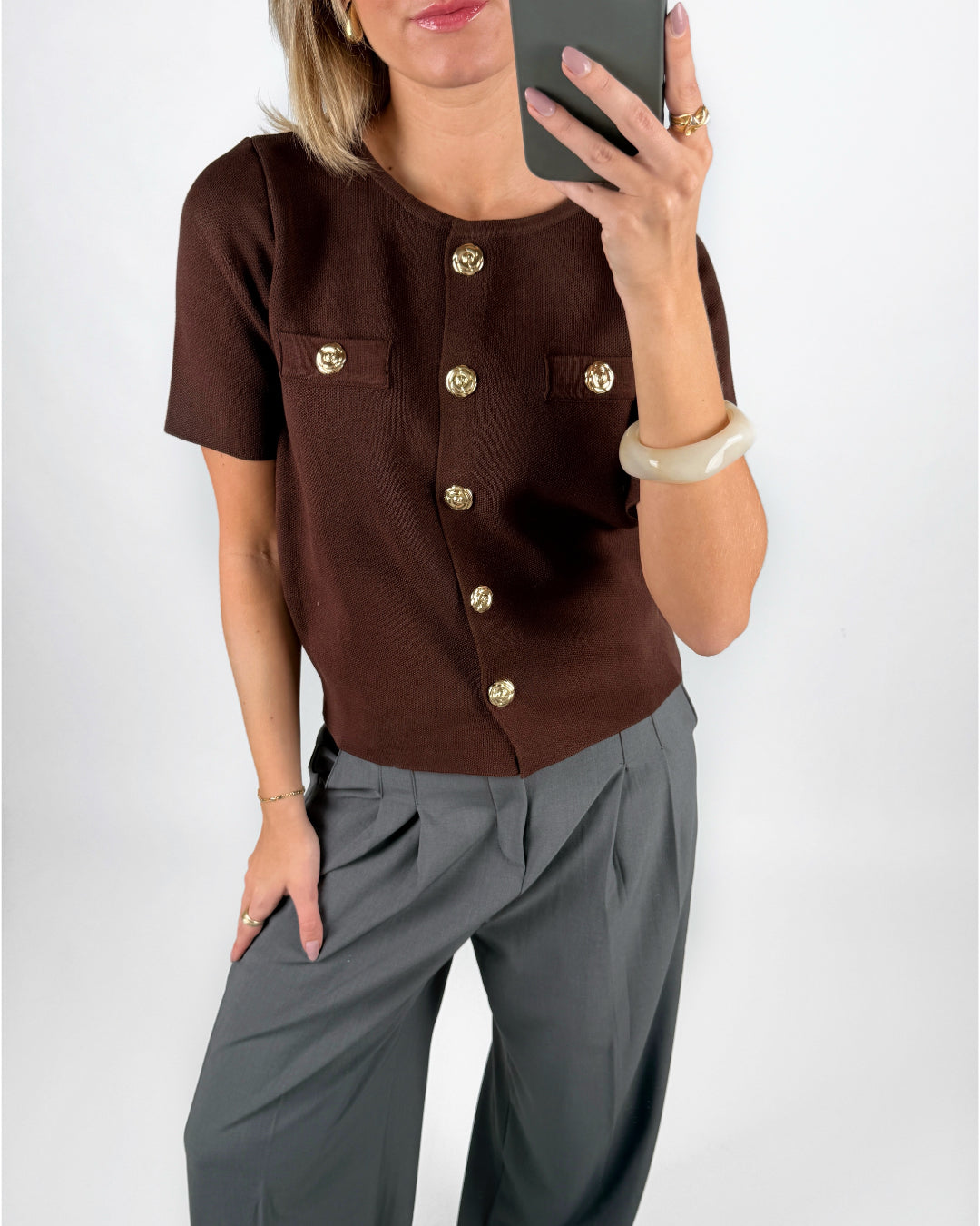 Modelfoto af pige i brun SIDNEY strik med guldfarvede knapper, samt grå LISA bukser. Alt er fra BySofieSønderby.