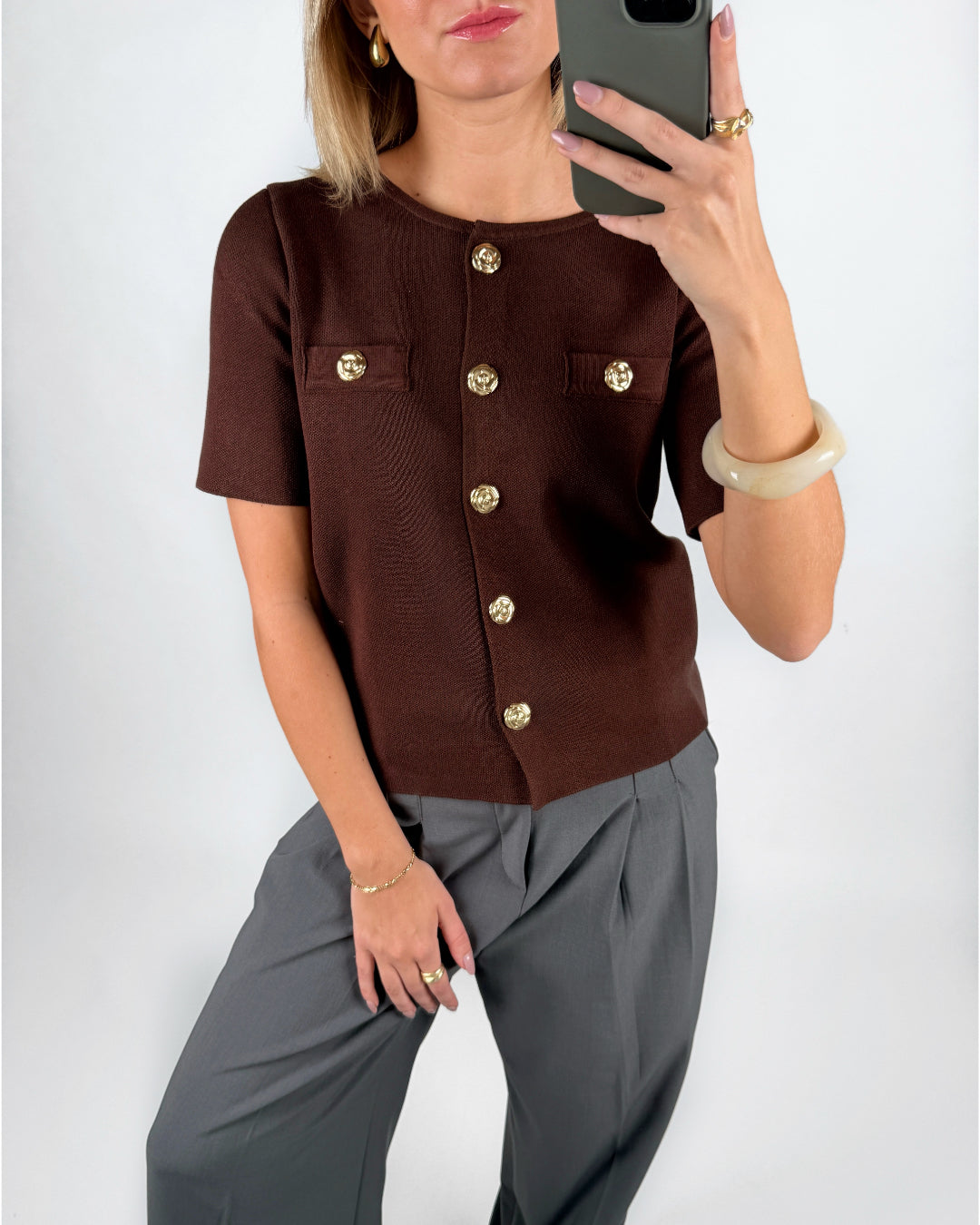 Modelfoto af pige i brun SIDNEY strik med guldfarvede knapper, samt grå LISA bukser. Alt er fra BySofieSønderby.