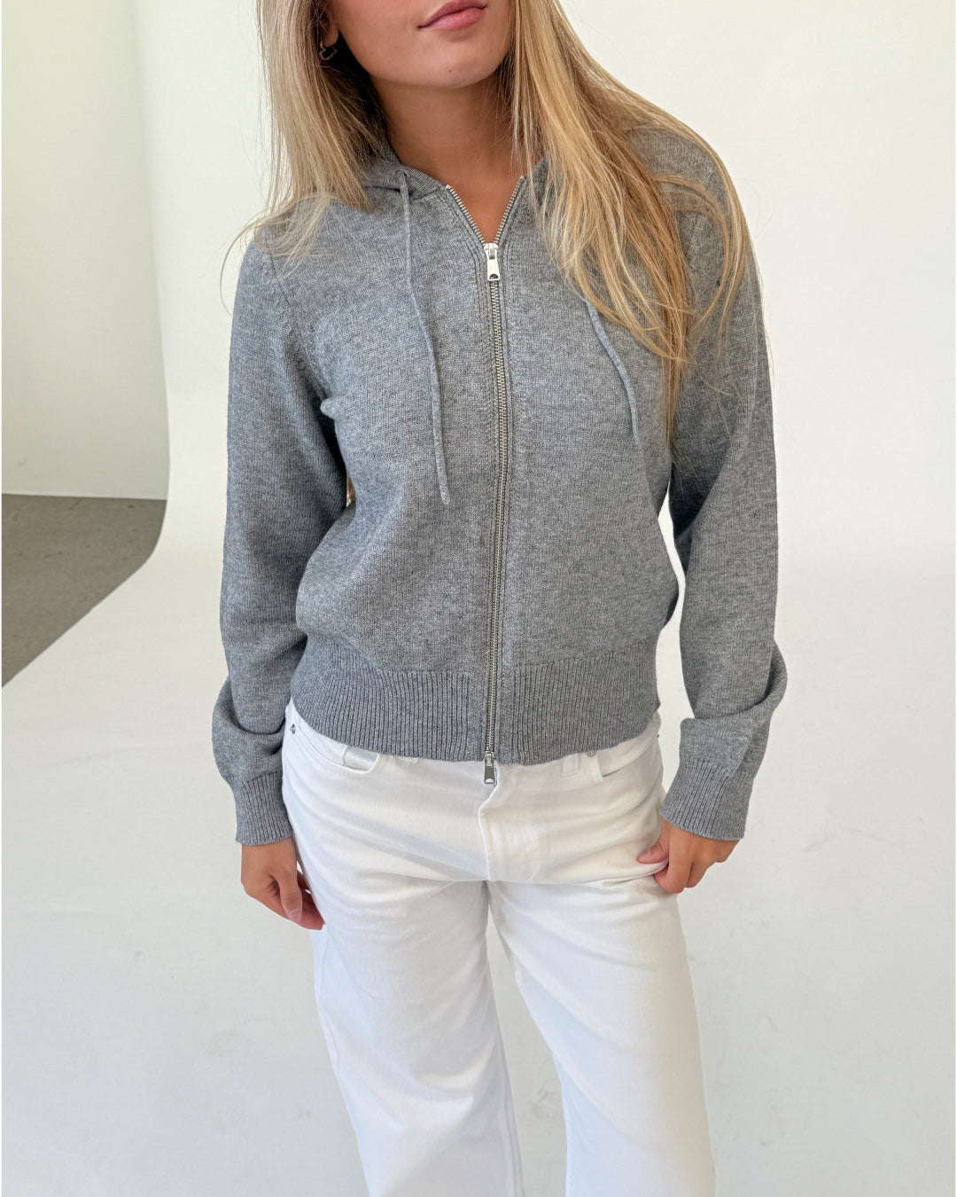 Modelfoto af pige i grå THESS  strik hoodie, samt hvide NANNA jeans. Alt er fra BySofieSønderby.