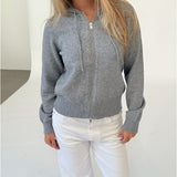 Modelfoto af pige i grå THESS  strik hoodie, samt hvide NANNA jeans. Alt er fra BySofieSønderby.