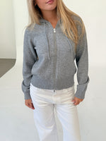 Modelfoto af pige i grå THESS  strik hoodie, samt hvide NANNA jeans. Alt er fra BySofieSønderby.