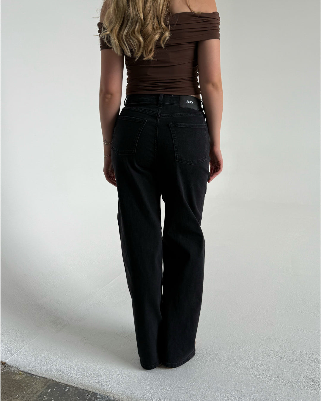 Modelfoto af pige som bærer et par sorte Tokyo jeans, samt iført en brun Thora one shoulder top. Alt fra By Sofie Sønderby