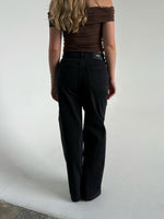 Modelfoto af pige som bærer et par sorte Tokyo jeans, samt iført en brun Thora one shoulder top. Alt fra By Sofie Sønderby