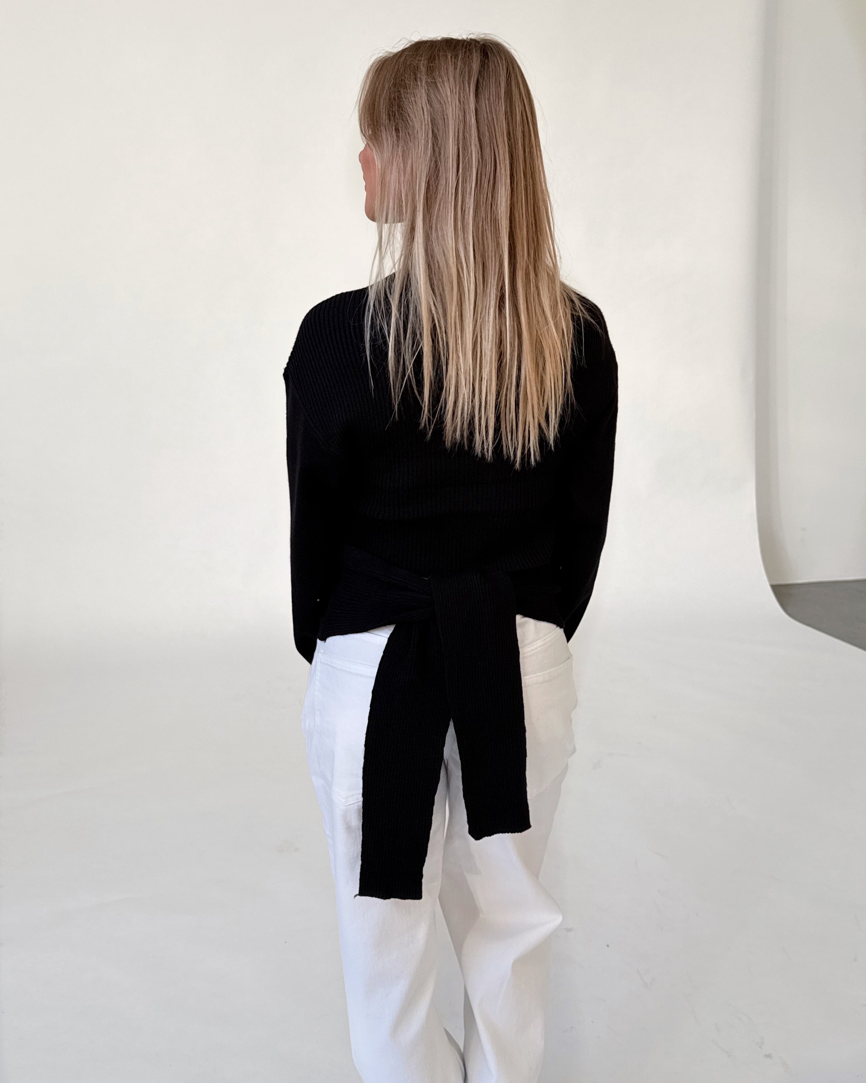 Modelfoto af pige i sort WHITNEY strik, samt hvide NANNA jeans. Alt er fra BySofieSønderby.