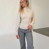 Modelfoto af pige i beige WHITNEY strik, samt grå NANNA jeans. Alt er fra BySofieSønderby.